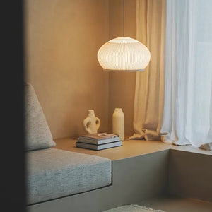 Lampada Knit Vibia sospesa sopra tavolino vicino al divano in ambiente residenziale moderno con luce calda.