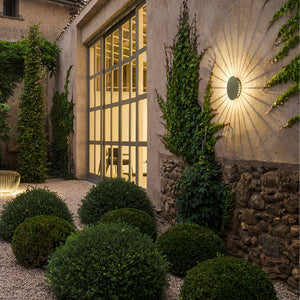 applique Meridiano che illumina un giardino di sera, creando un'atmosfera calda e suggestiva.