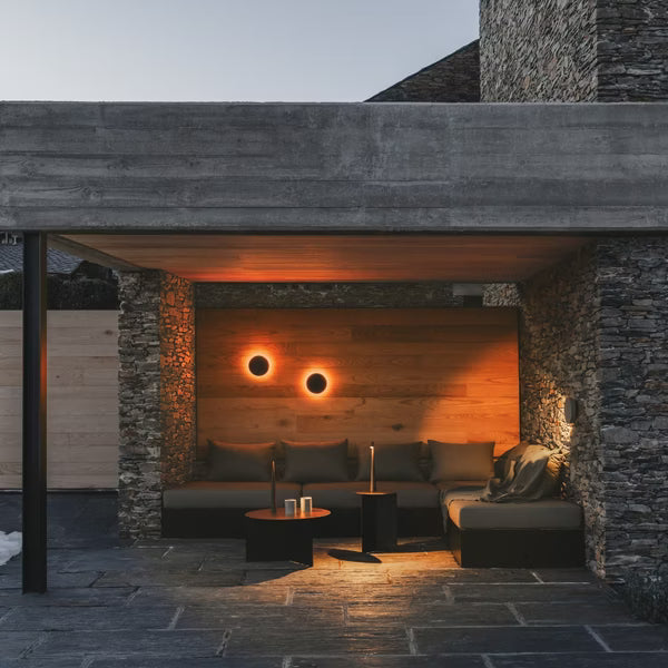 Serie di applique Dots Outdoor 4684 che creano un'aureola di luce per illuminare una terrazza in legno e pietra.