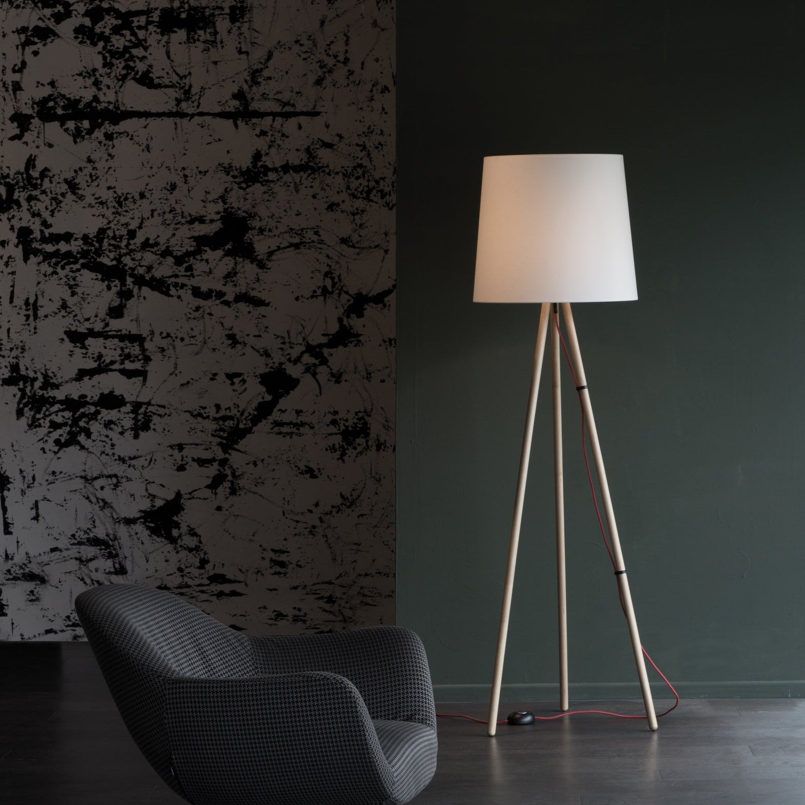 Lampada da terra con treppiede Eva di Martinelli Luce con diffusore bianco posizionata in un soggiorno moderno.