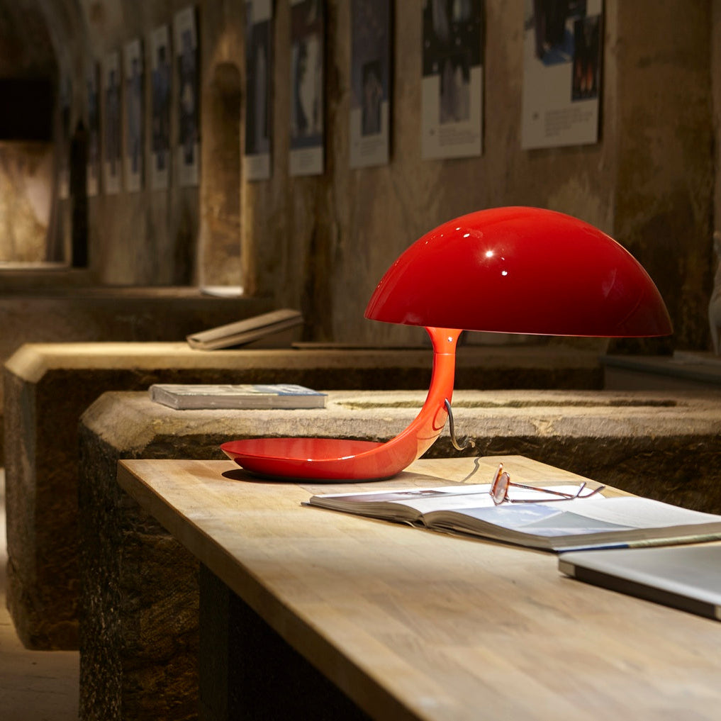 iconica lampada Cobra rossa con la base ruotata su un tavolo.
