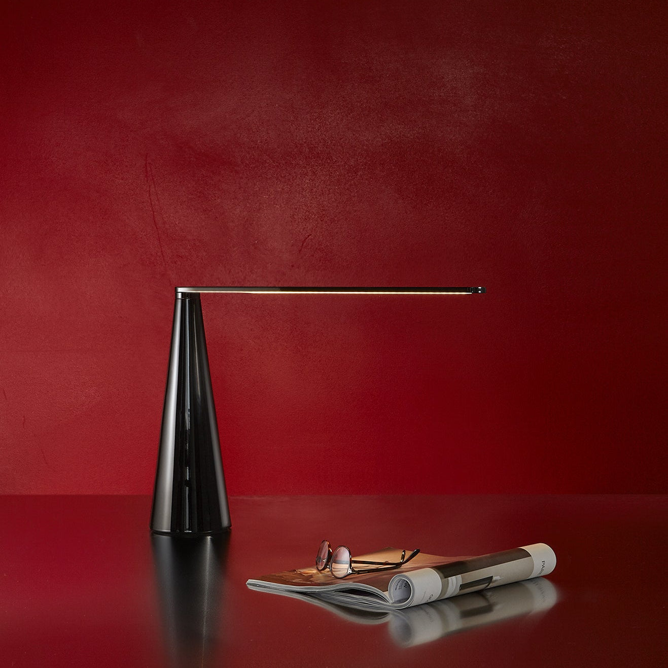 Lampada da scrivania Elica di Martinelli Luce che illumina una superficie moderna e minimale.