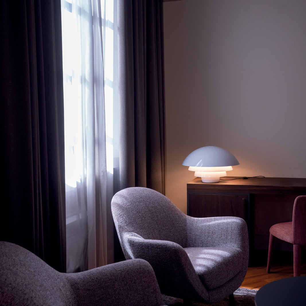 Lampada da tavolo Visiere di Martinelli Luce posizionata su una credenza in un soggiorno, che crea una luce indiretta d'atmosfera.