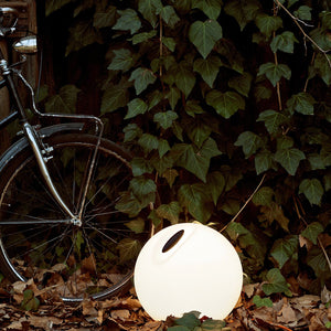 Lampada d'apoggio Bowl posizionata in un'aiuola con intorno foglie cadute. 
