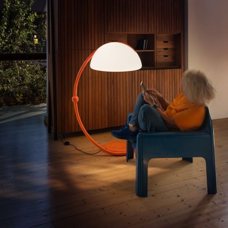 Iconica lampada Serpente 60 che illumina un angolo lettura con il suo colore arancione.