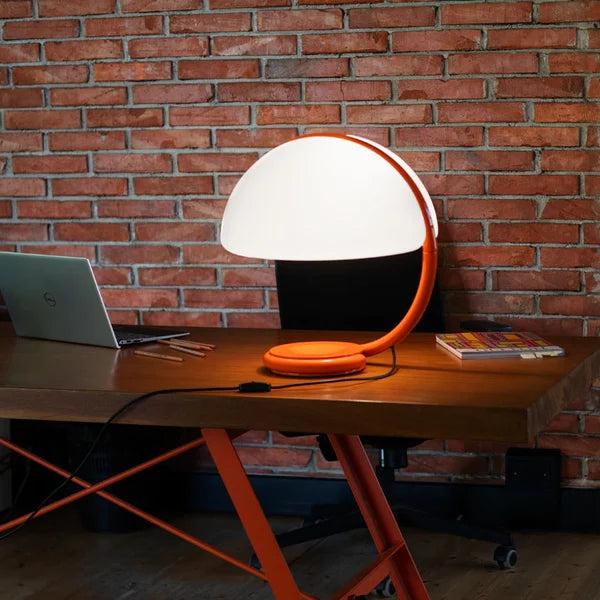 Lampada di design Serpente 60 arancione su una scrivania moderna.